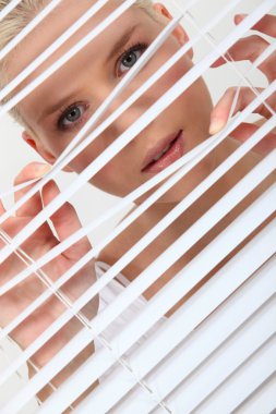 Woman peering through some blinds clipart