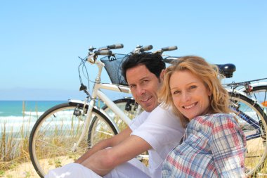 Couple on holiday sitting in front of bicycles clipart