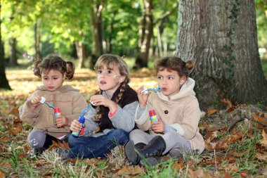 Three little girls playing with soap bubble solutions in the forest clipart