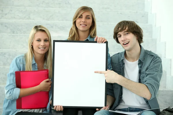 Três estudantes segurando uma prancha deixaram em branco para sua imagem — Fotografia de Stock