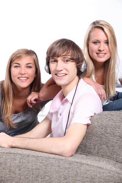 Um menino ouvindo música e duas meninas loiras atrás de um sofá — Fotografia de Stock
