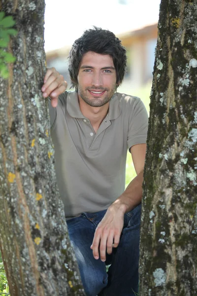 25 anos de idade homem agachado em seus saltos atrás de duas árvores — Fotografia de Stock