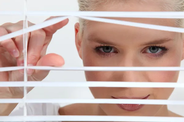 Een blonde vrouw kijkt door blinds — Stockfoto