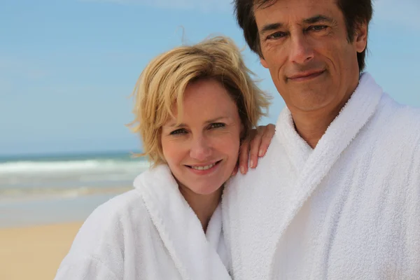 Casal vestindo roupões de banho brancos em pé junto ao mar — Fotografia de Stock