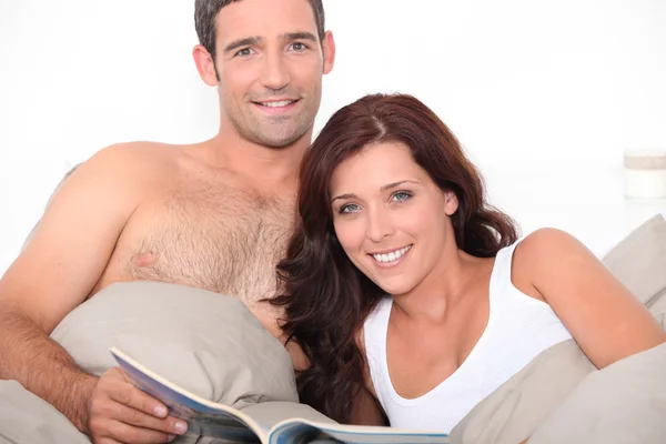 Paar liest Zeitschrift im Bett — Stockfoto