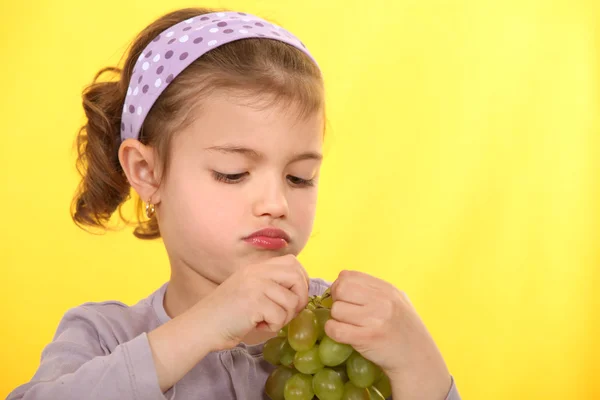 En liten flicka som äter vindruvor. — Stockfoto