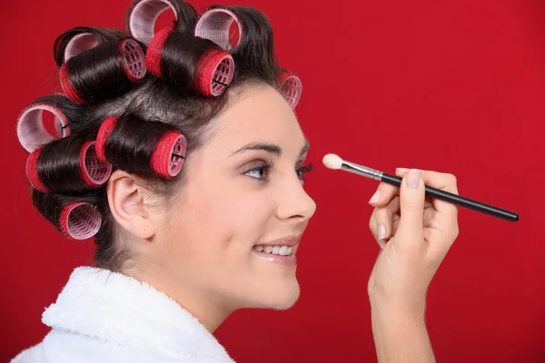 Woman with hair curlers applying make-up — Stock Photo, Image
