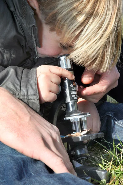 Любопытный маленький мальчик использует микроскоп на открытом воздухе — стоковое фото