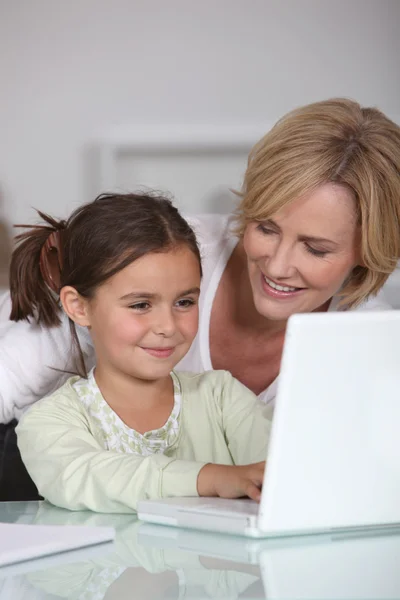 Madre e giovane figlia utilizzando un computer portatile bianco insieme — Foto Stock