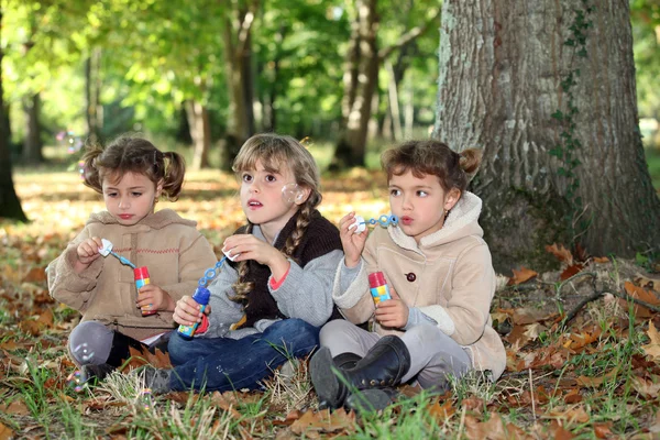 Tres niñas jugando con soluciones de burbujas de jabón en el bosque —  Fotos de Stock