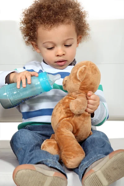 Мальчик кормит плюшевого мишку из бутылки — стоковое фото