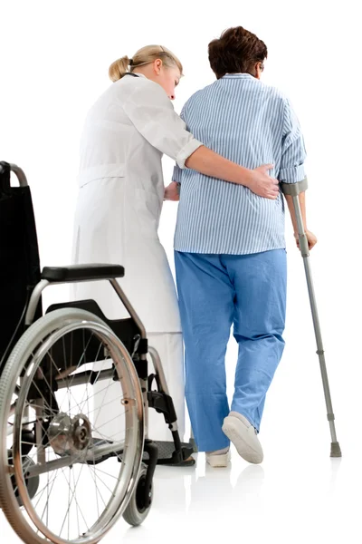 Verpleegkundige helpt een senior vrouw op krukken — Stockfoto