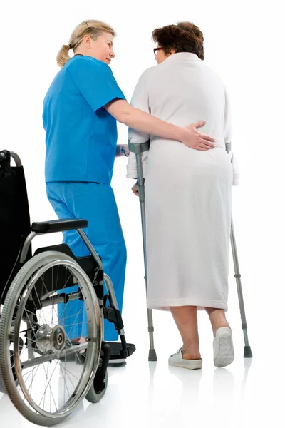 Enfermera ayuda a una mujer mayor en muletas — Foto de Stock