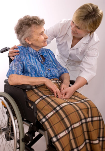 Молодая медсестра поощряет пожилую женщину в инвалидном кресле
