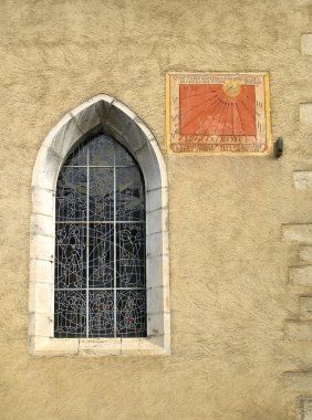 Anciant church window with sun dial on a stone wall clipart