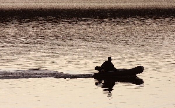 Silhouette of a man in a boat on the water, the trace of the boat