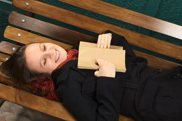 Junge glückliche Frau liegt auf Bank und liest — Stockfoto
