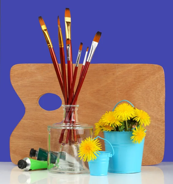 Brushes with the palette and dandelions — Stock Photo, Image