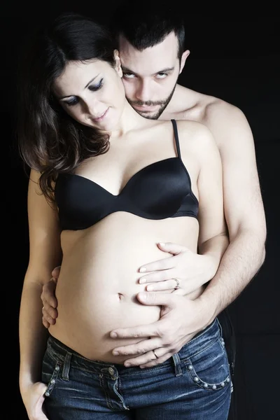 Gelukkig zwangere en vader op zwarte achtergrond strelen van de klok — Stockfoto
