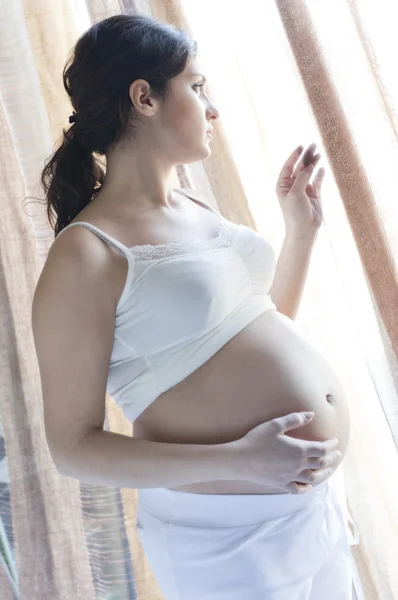 Pregnant woman that looks out the window — Stock Photo, Image