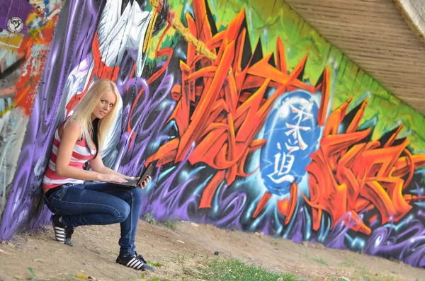Girl against a wall with graffiti and laptop — Stock Photo, Image