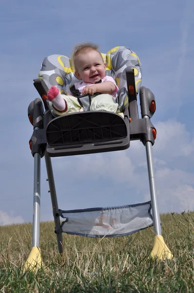 Niña sentada en silla de bebé comiendo en la naturaleza —  Fotos de Stock