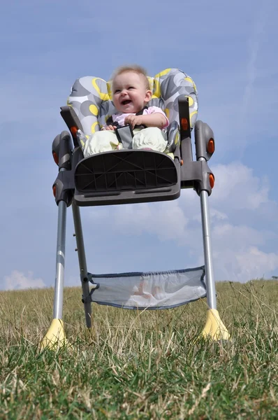 Niña sentada en silla de bebé comiendo en la naturaleza —  Fotos de Stock