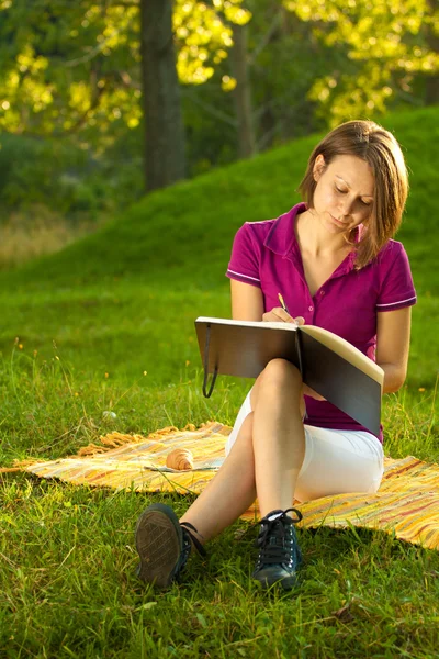 Beautiful woman writing in her diary in the park — Stock Photo, Image