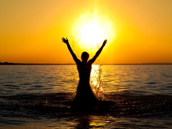 Zwemmer springen uit zeewater op gouden zonsondergang — Stockfoto