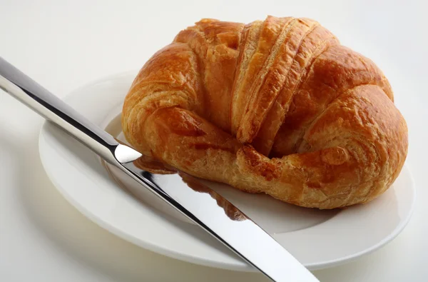Croissant, white plate and knife — Stock Photo, Image