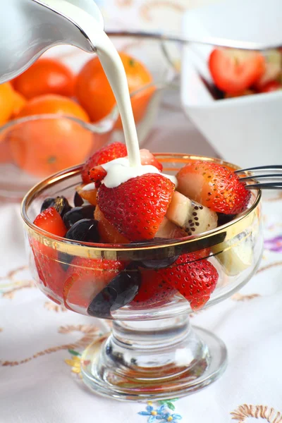 Cream being poured on Fresh fruit salad in a glass bowl — Stock Photo, Image