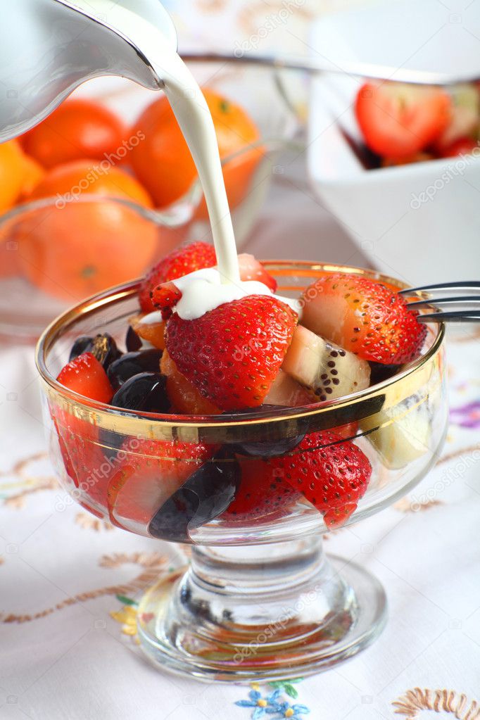 Cream being poured on Fresh fruit salad in a glass bowl