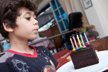 Boy blowing out candles on a slice of chocolate cake clipart