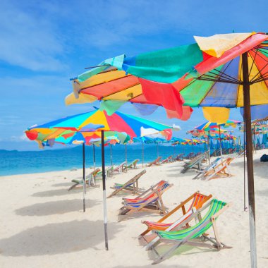 Colorful sun parasols and sundeck chairs on beautiful white sandy beach clipart