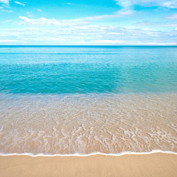 Hermosa playa de arena con aguas tranquilas contra cielos azules . — Foto de Stock