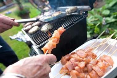 Chicken kebabs and burger meat patties being grilled clipart