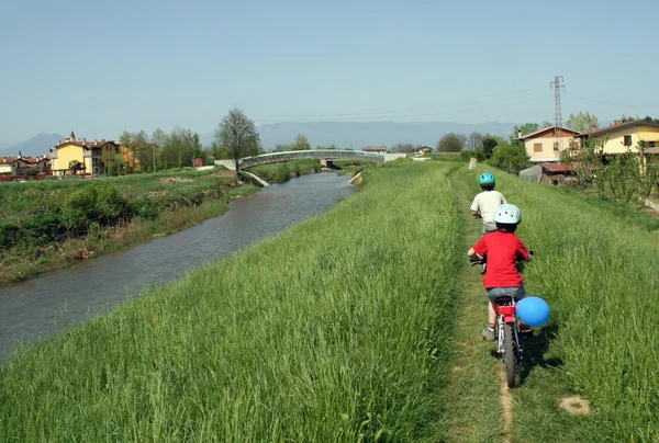 Children cycling on a small trail of a bank of a river in spring — Stock Photo, Image