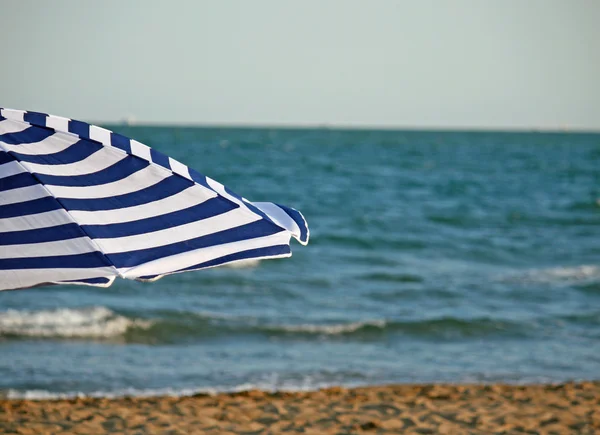 Ombrellone a righe sulla spiaggia e sul mare sullo sfondo — Foto Stock