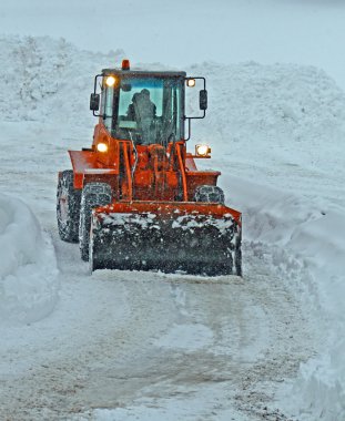 Orange snow plow clears the streets during a snow storm clipart