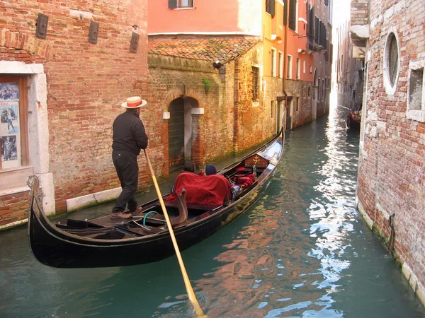 Gondolier in a gondola along a canal through the houses of Venice — Stock Photo, Image