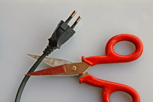 Tesoura que corta o cabo elétrico de um plugue preto — Fotografia de Stock