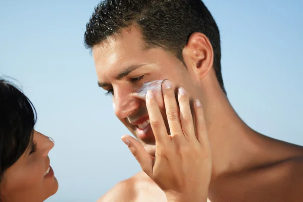 Couple on the beach putting on cream — Stock Photo, Image