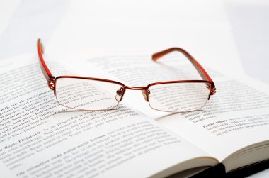 Reading glasses lying on the open book clipart