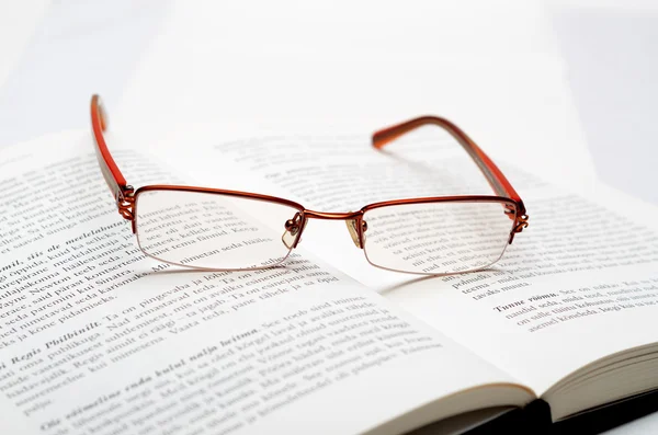 A nyitott könyvön fekvő olvasószemüveg Stock Kép
