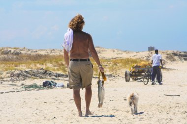 Man walking on the beach with his dog and a freshly fished fish clipart