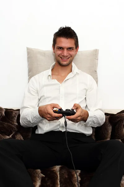 Leende spelare sitter på soffan med controller och spela — Stockfoto