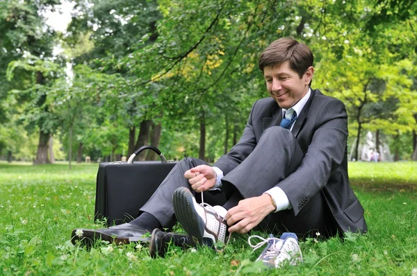 Homem de negócios sênior mudando sapatos no parque — Fotografia de Stock
