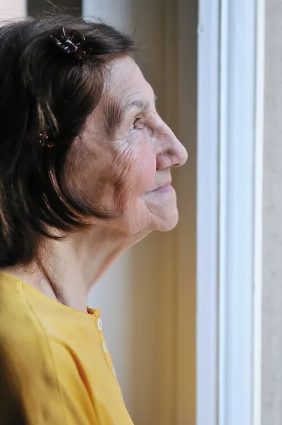 Solidão - mulher sênior olhando através da janela — Fotografia de Stock