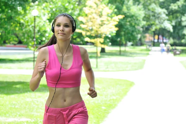 Mujer joven con auriculares corriendo en el parque — Foto de Stock