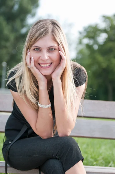 Młoda kobieta uśmiechający się usytuowanie na ławce na zewnątrz — Zdjęcie stockowe